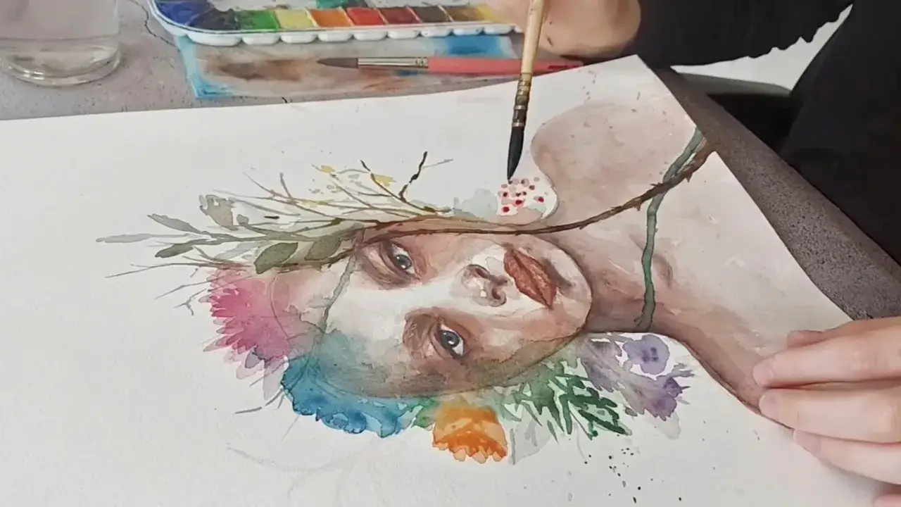 Composition aquarelle d'un visage f&eacute;minin orn&eacute; de fleurs et de feuillages, une main tenant un pinceau ajoute des touches de couleur.