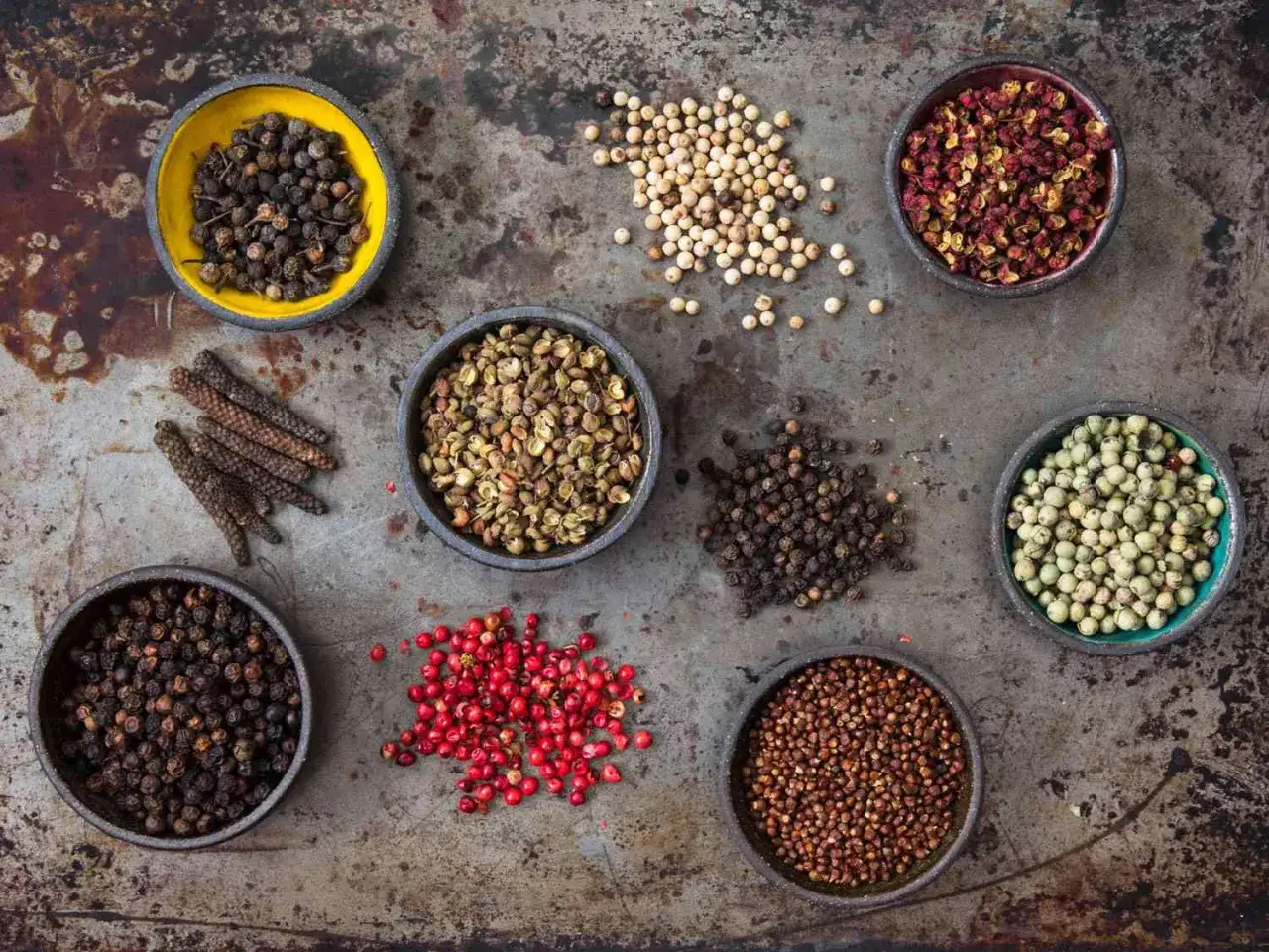 Verschiedene Pfeffersorten in Schalen und verstreut. Von schwarzem bis weißem Pfeffer, Long Pepper und Sichuanpfeffer – hier sieht man, woher Pfeffer kommt.