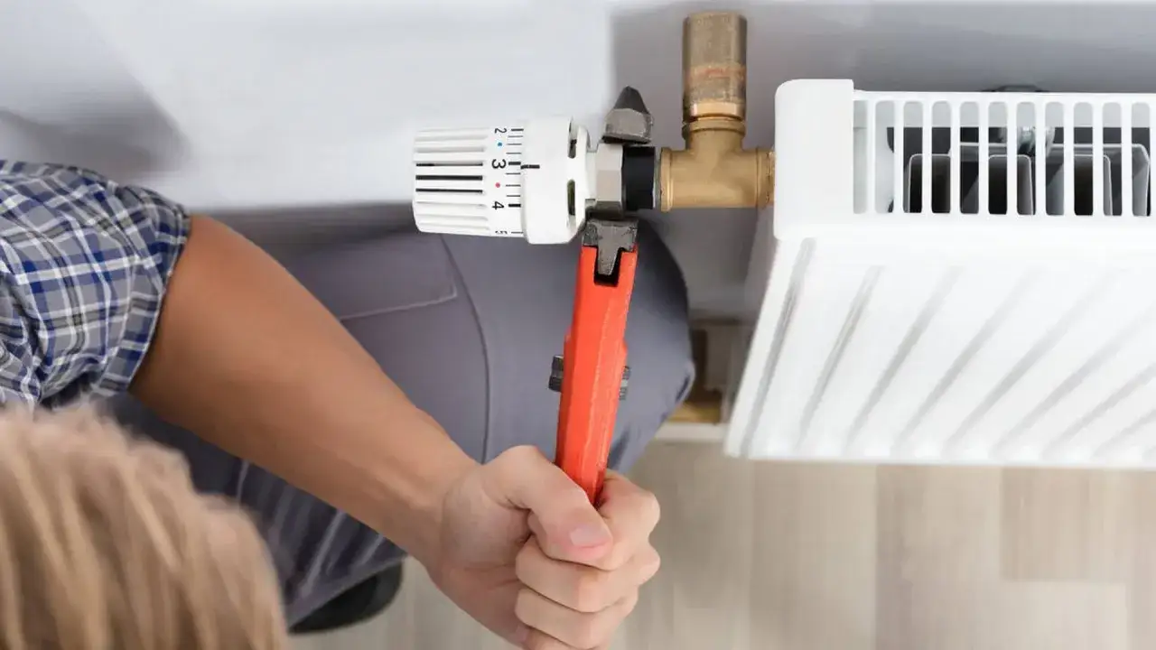 Hand mit Zange dreht am Heizkörperthermostat. Ein Handwerker hilft beim Thermostat wechseln.