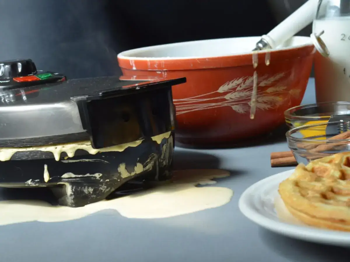 Ein überlaufendes Waffeleisen sorgt für Chaos. Teig tropft herunter, was die Reinigung erschwert.