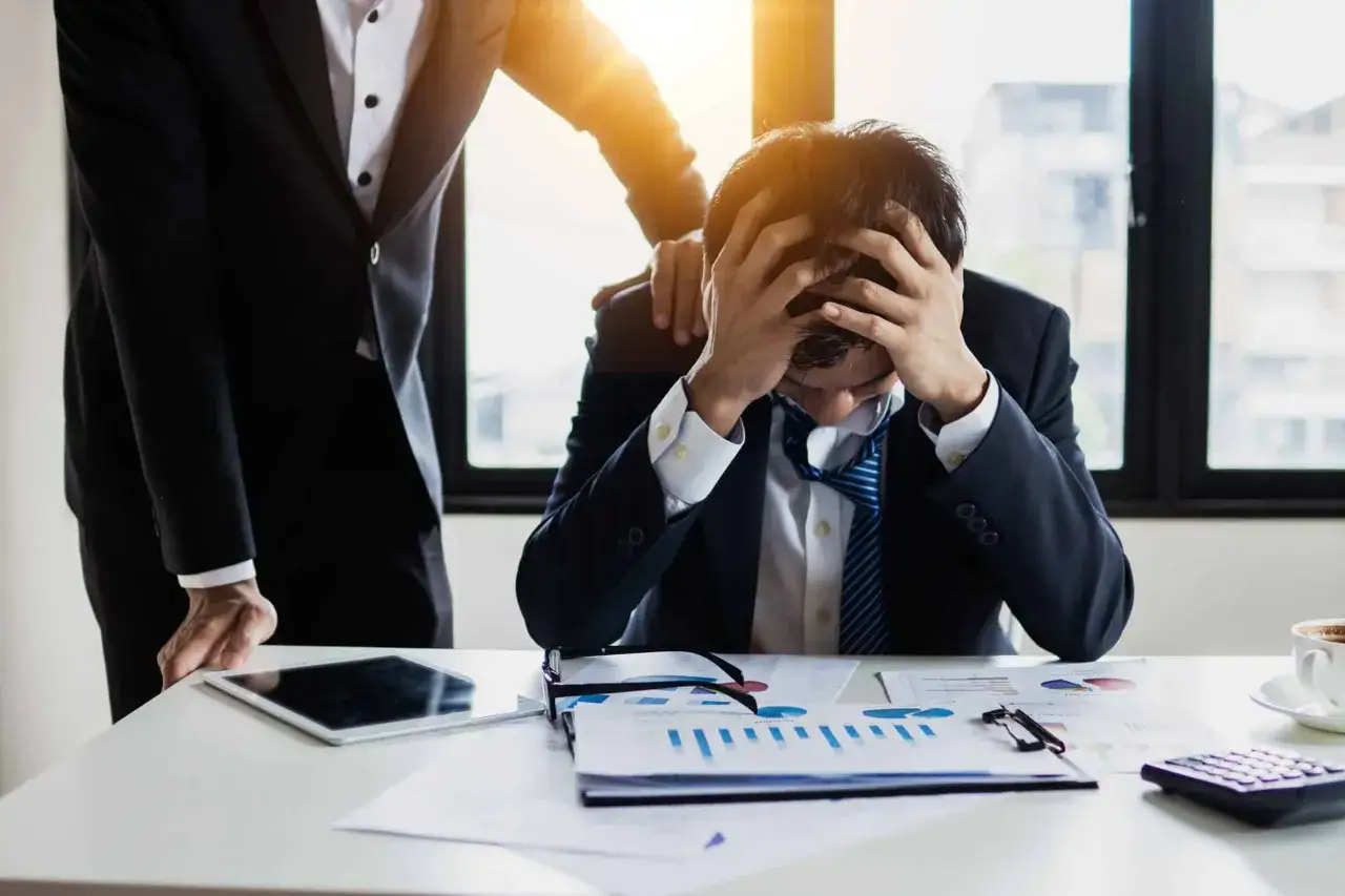 Un homme d'affaires d&eacute;sesp&eacute;r&eacute;, accabl&eacute; par le stress, re&ccedil;oit une tape sur l'&eacute;paule. L'ambiance sugg&egrave;re un management toxique.