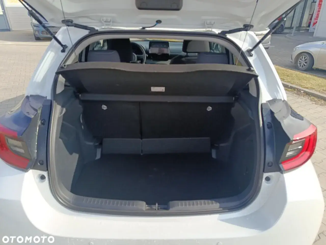 Biała Toyota Yaris używana z salonu, z otwartym bagażnikiem. Idealna na rodzinne wyjazdy.