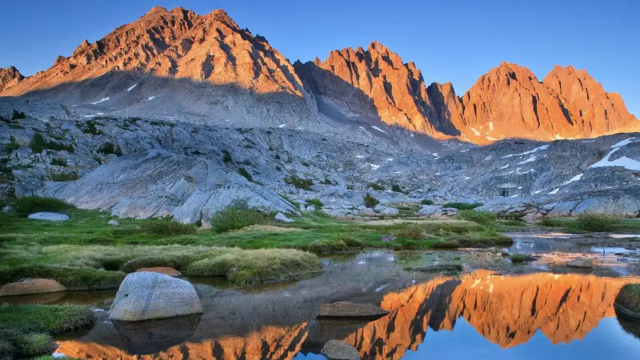 Złote słońce oświetla ostre szczyty Sierra Nevada, odbijając się w spokojnej wodzie.