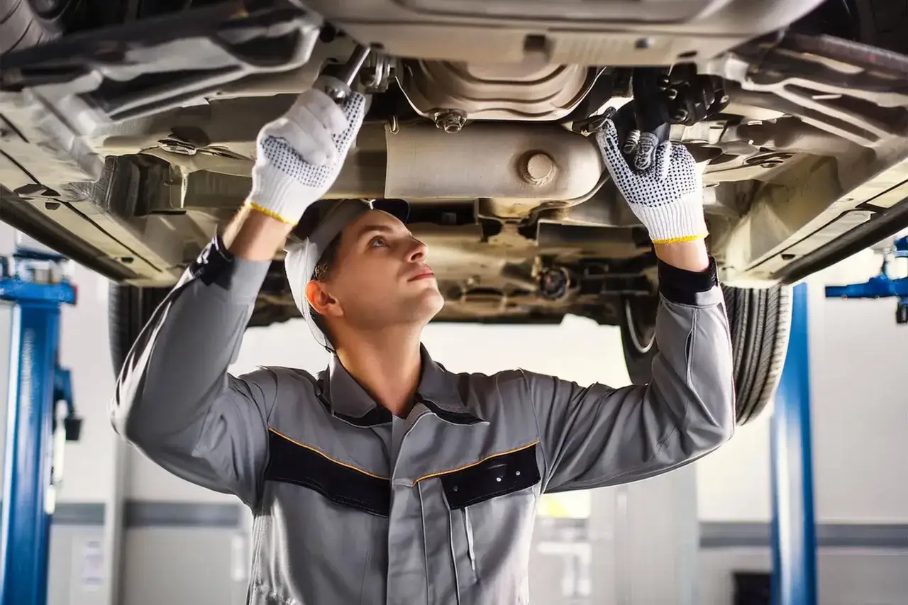 Mécanicien concentré sous une voiture, gants blancs, pour tester capteur ABS.