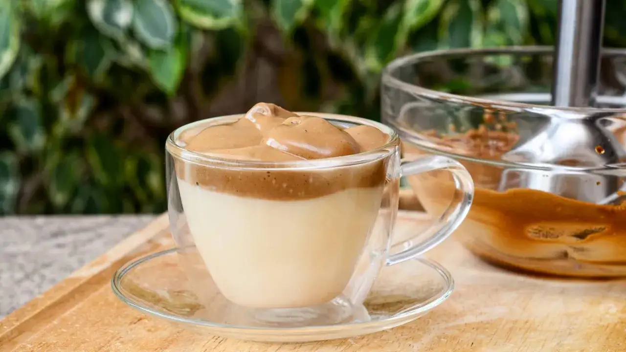 En krämig dalgona kaffe i ett glas med dubbla väggar, toppad med vispad kaffemassa.