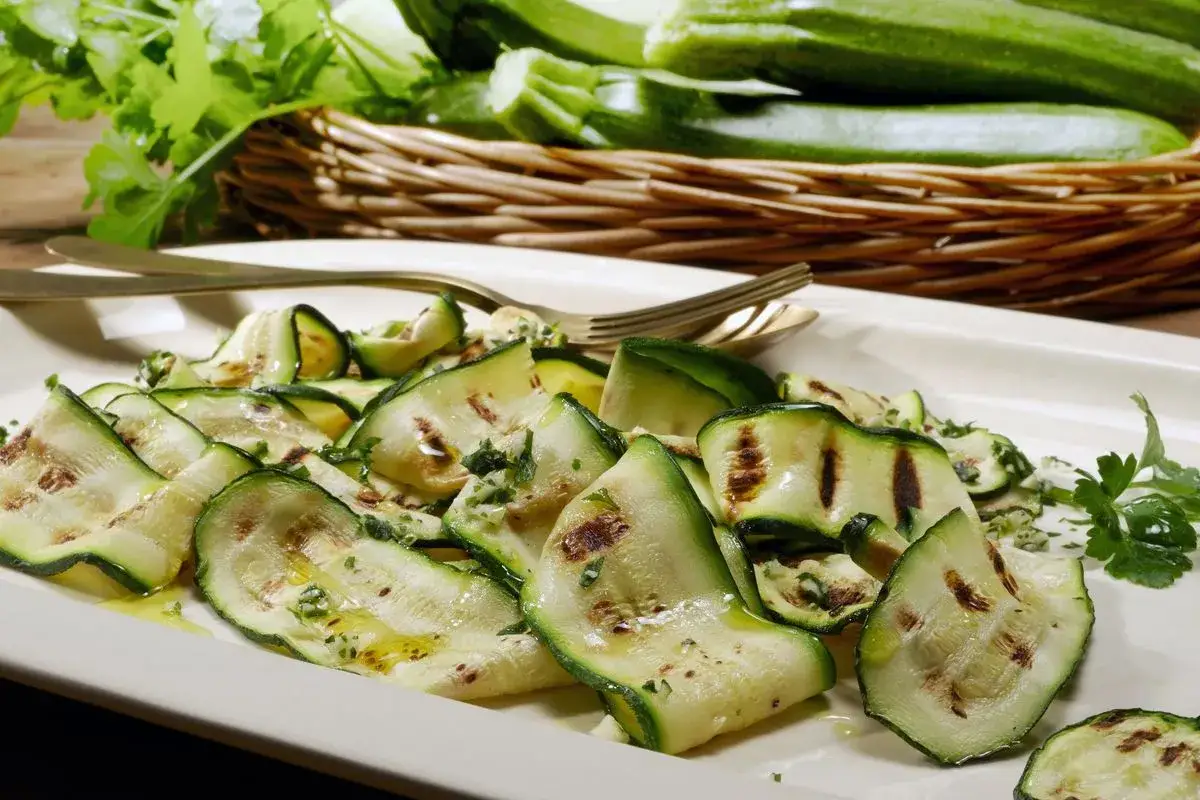 Fette di zucchine marinate cotte, condite con olio e prezzemolo, servite su un piatto bianco.