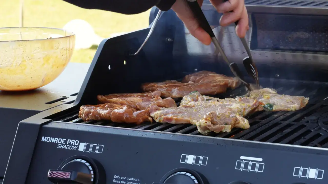 Karkówka na grillu elektrycznym skwierczy, a dym unosi się w powietrze. Ręka z szczypcami obraca soczyste kawałki mięsa, przygotowując je do podania.