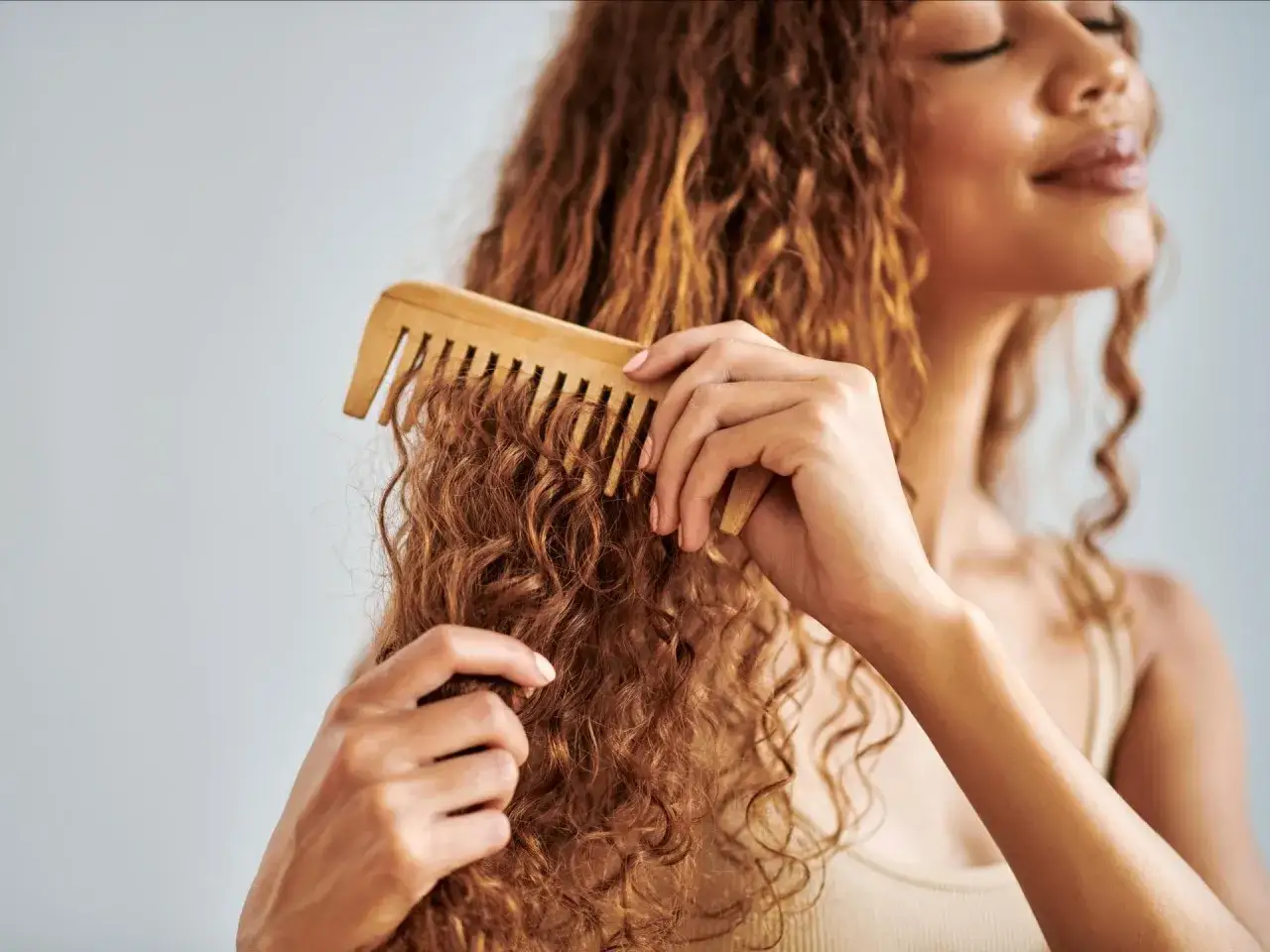 Frau k&auml;mmt sanft ihre vollen, roten Locken mit einem Holzkamm. So lassen sich Locken richtig pflegen und Frizz vermeiden.