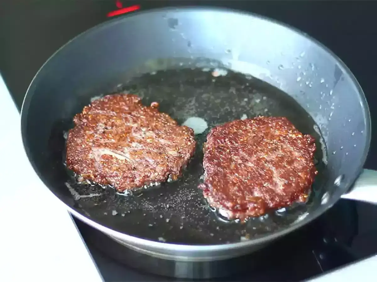 Två gyllenbruna vegetariska biffar steks i en stekpanna med olja.