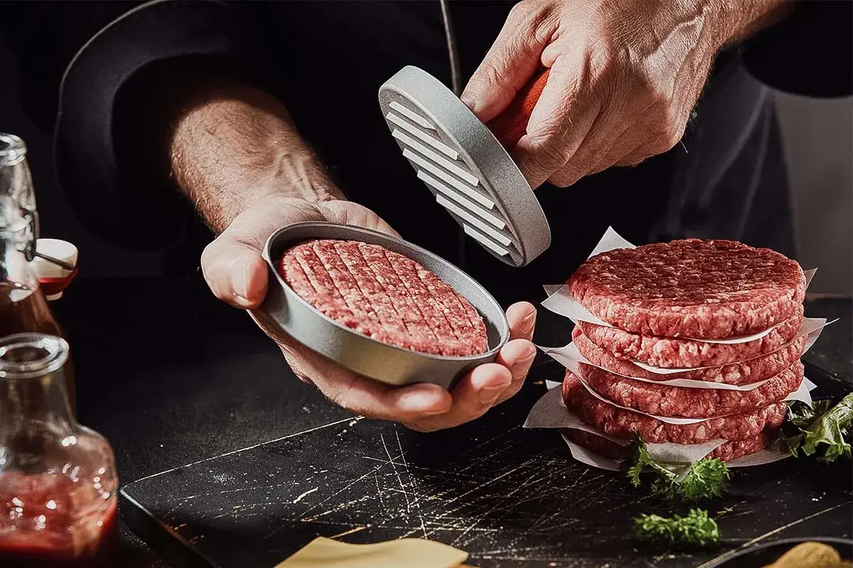 Frische burger patties werden mit einem Patty-Former geformt. Ein Stapel fertiger burger patties liegt daneben.