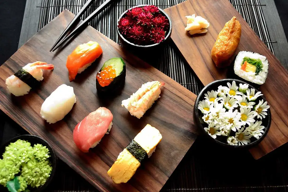Wyśmienite japońskie jedzenie: sushi z krewetką, łososiem, tuńczykiem, ikrą, tamago i inari. Udekorowane kwiatami i marynowanym imbirem.