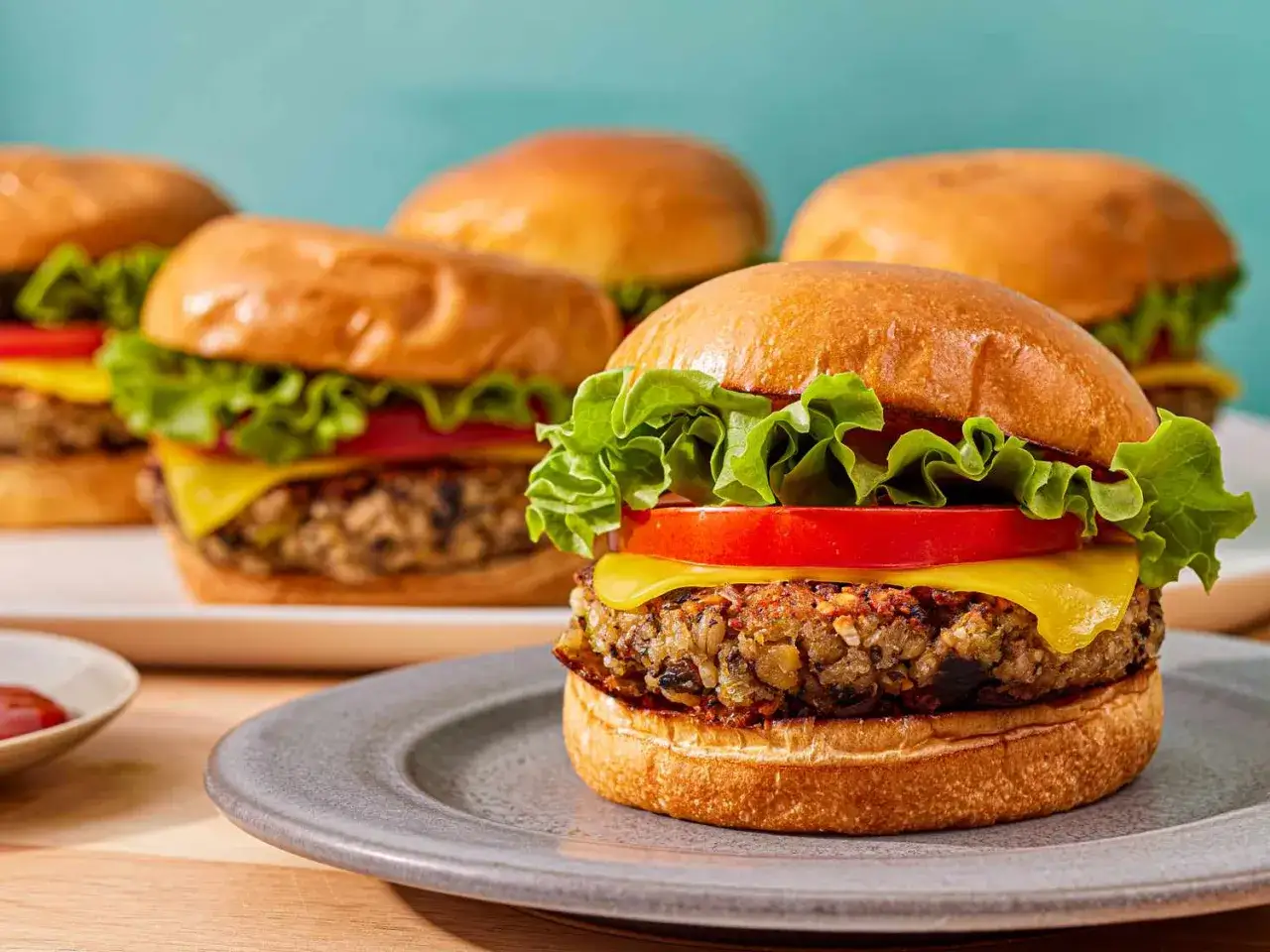 Saftige vegetarische Burger mit Salat, Tomate und Käse auf einem Teller. Im Hintergrund weitere Burger.