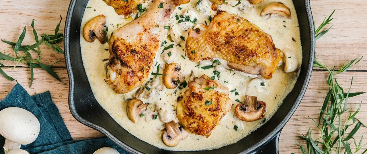 Poulet r&ocirc;ti en sauce cr&eacute;meuse avec champignons dans une po&ecirc;le.