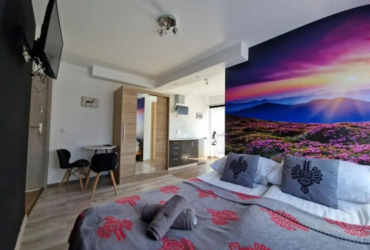 Pokoje i apartamenty Wierchy Zakopane: przytulne wnętrze z widokiem na g&oacute;ry na fototapecie, ł&oacute;żko z g&oacute;ralskimi akcentami, aneks kuchenny i szafa.