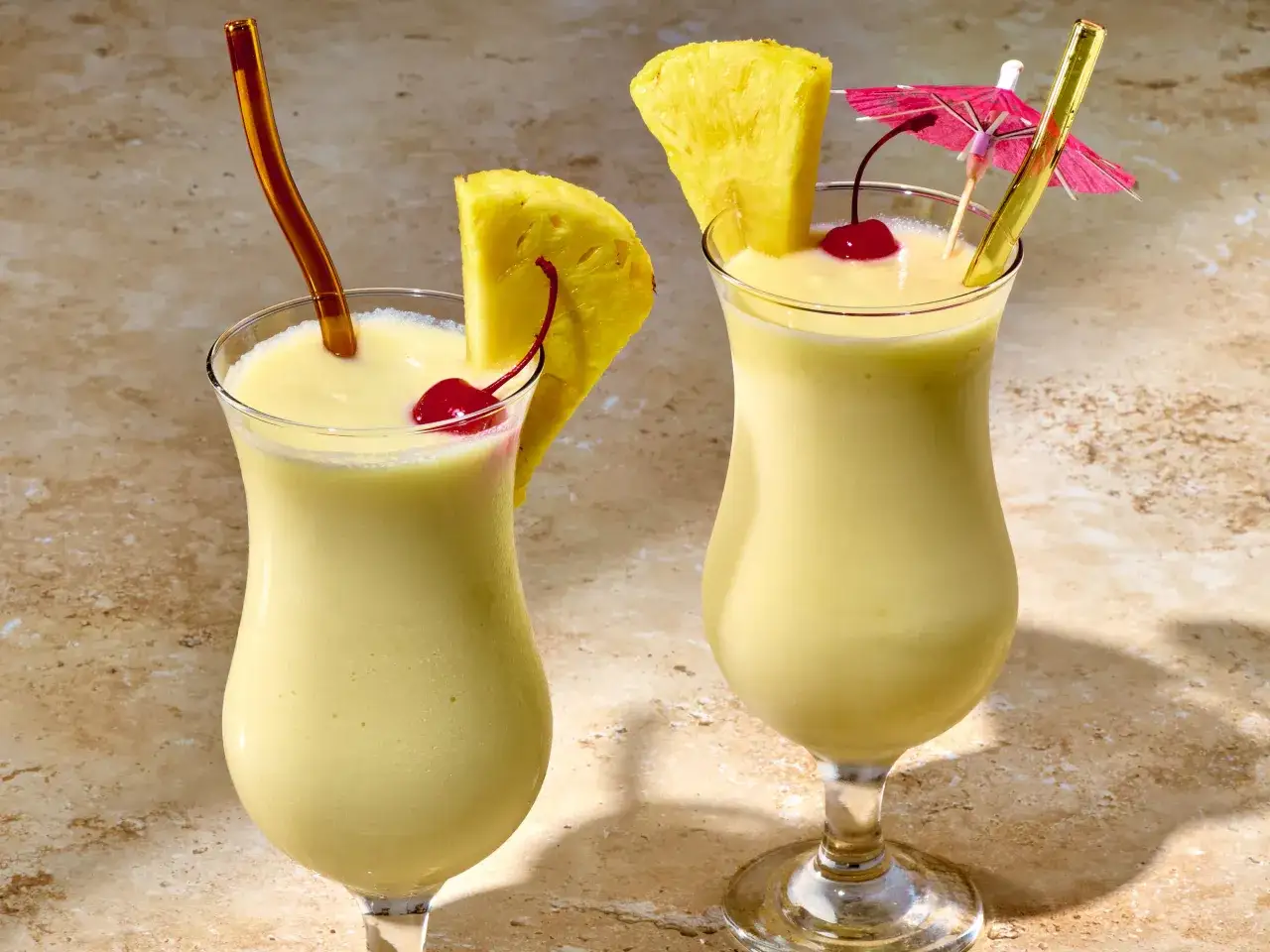 Två glas med krämig pina colada, garnerade med ananasskivor och körsbär. Perfekt för en solig dag!