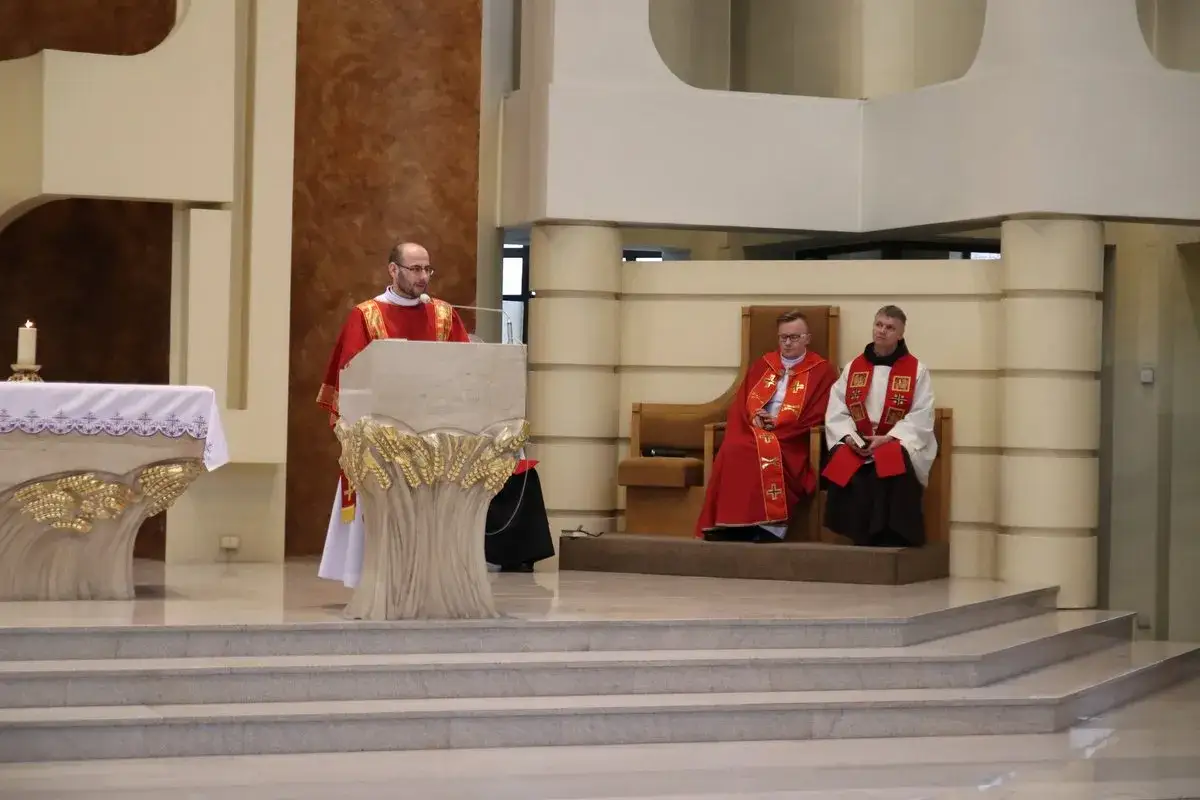 W kościele trwa nabożeństwo. Ksiądz przy pulpicie, dwaj duchowni siedzą.