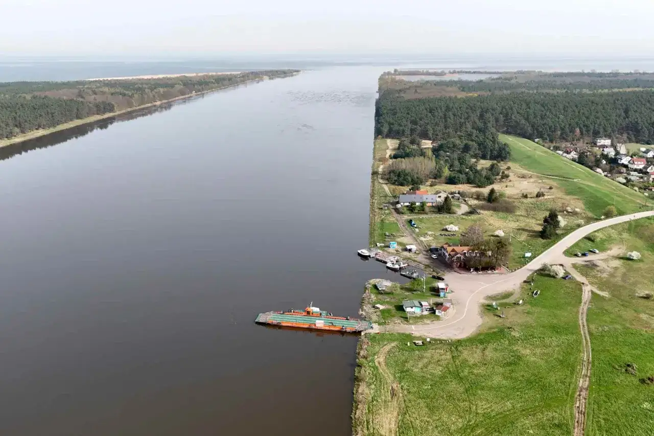 Prom Mikoszewo-Świbno przewozi pasażerów przez szeroką rzekę, otoczoną lasami i zielonymi łąkami.