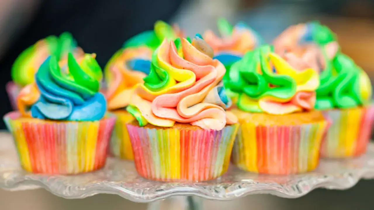 Bunte Muffins mit Lebensmittelfarbe, die wie ein Regenbogen aussehen, auf einem Glasst&auml;nder.