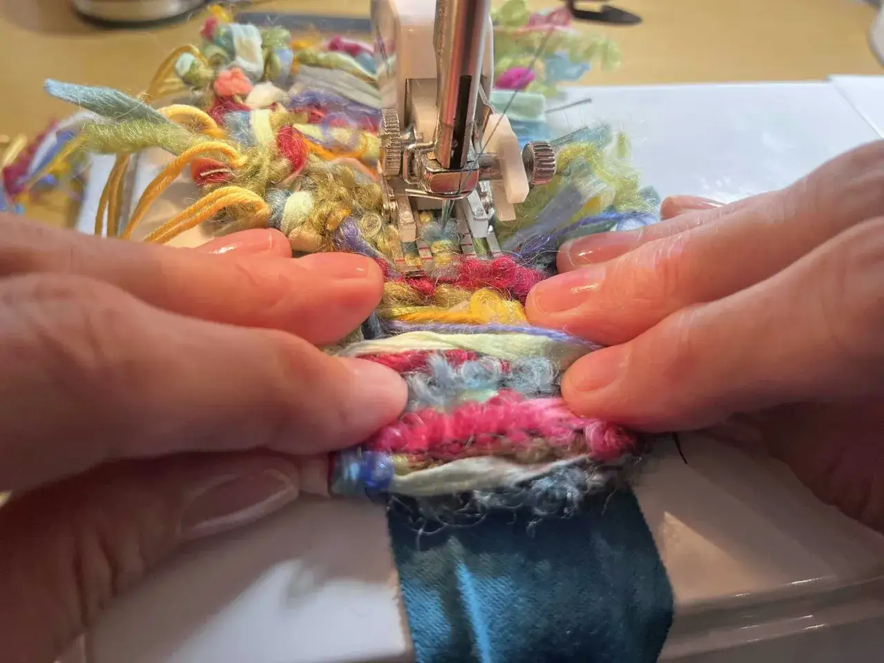 Hands guide colorful yarn through a sewing machine, demonstrating how to sew fringe for a unique textile project.