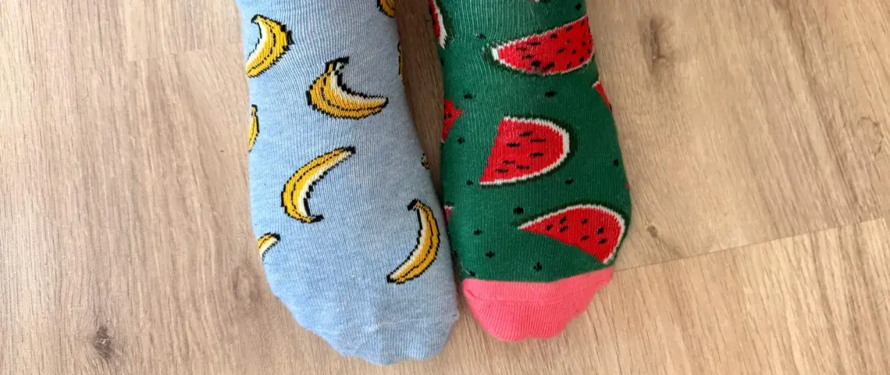 Dzień kolorowej skarpetki! Jedna w banany, druga w arbuzy. Wesołe wzory na drewnianej podłodze.