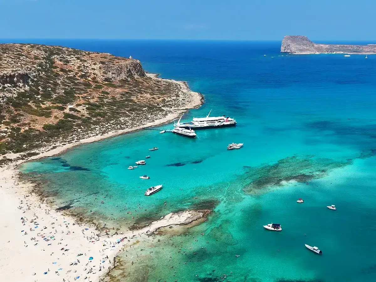 Rajska plaża z turkusową wodą, statkami i mn&oacute;stwem ludzi. Kreta wschodnia atrakcje zapierają dech w piersiach!