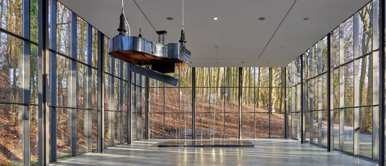 Ein schwebendes Klavier in der Villa Waldfrieden Wuppertal, umgeben von einem Wald aus Glas.