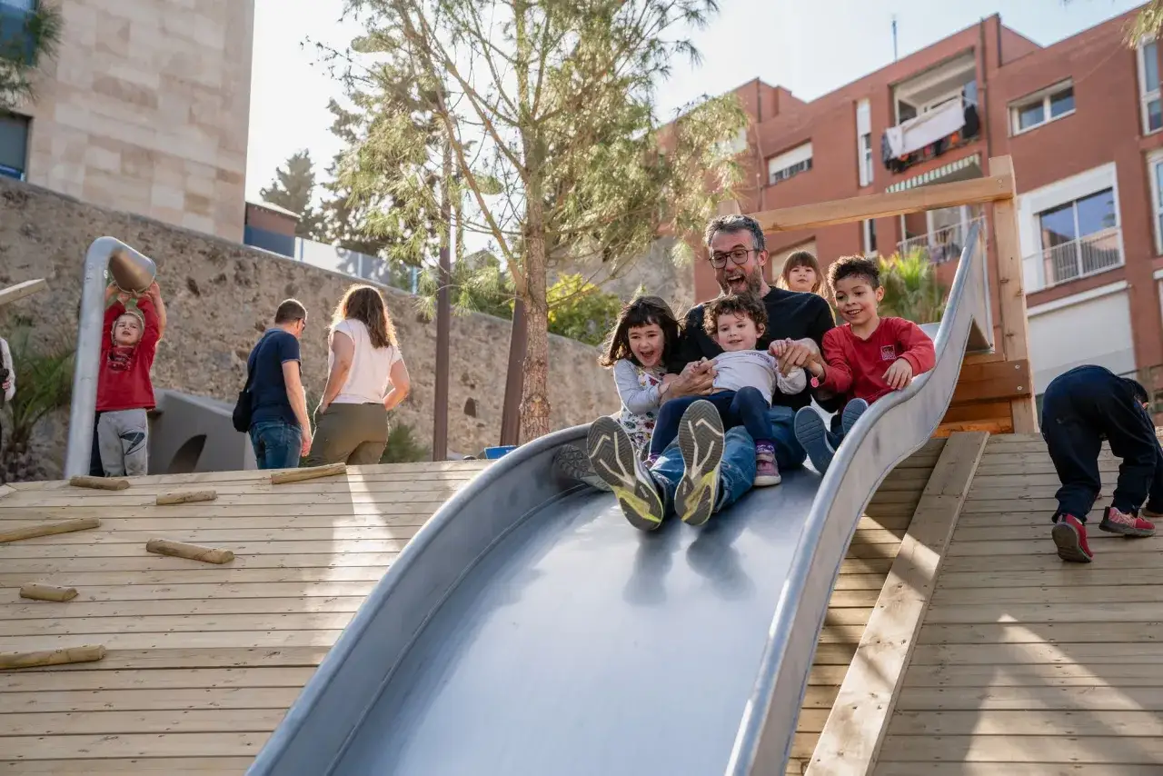 Padre y niños disfrutan de un tobogán en un parque, una idea genial de qué hacer con niños en Barcelona.