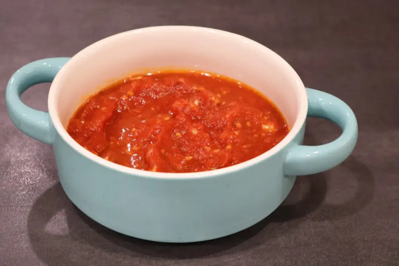 Un tazón azul claro con asas contiene una sabrosa salsa marinara, lista para acompañar pasta o pizza.