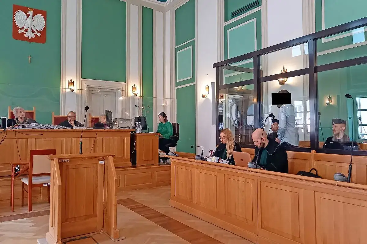 Sala sądowa, gdzie odbywa się proces. Sędziowie, prawnicy i oskarżony w kąciku. W tle godło Polski.
