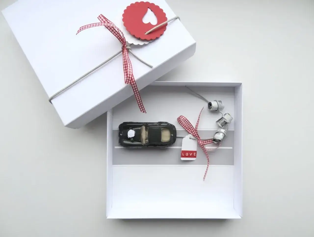Une boîte blanche ouverte révèle une petite voiture noire, des rouleaux de fil et une étiquette