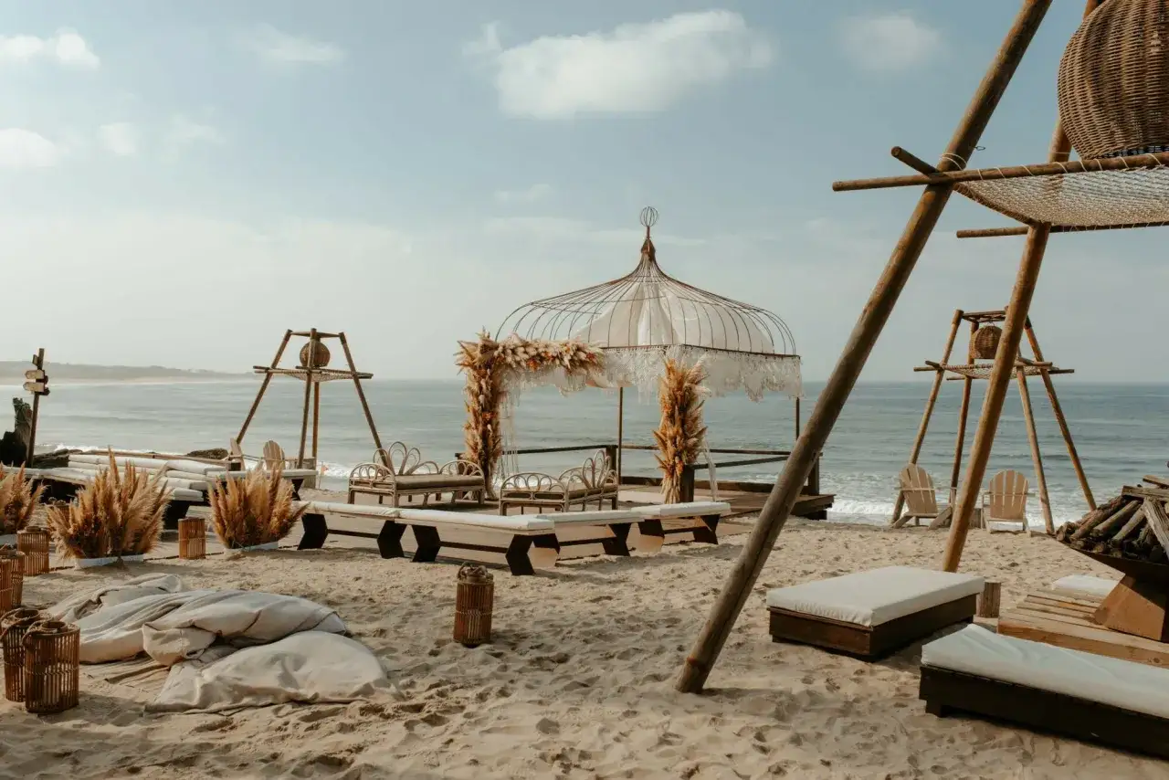 Un d&eacute;cor de r&ecirc;ve pour un mariage Portugal sur la plage, avec un dais orn&eacute; de pampas et des si&egrave;ges en rotin face &agrave; l'oc&eacute;an.
