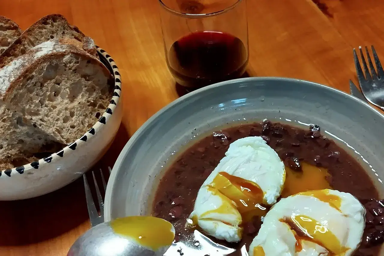 Un plat d'oeufs meurette avec du pain et un verre de vin rouge.
