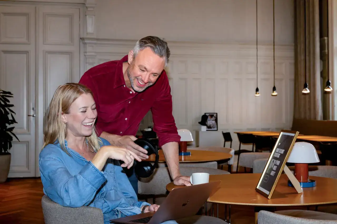 Tv&aring; glada kollegor diskuterar id&eacute;er vid ett bord. Mannen h&aring;ller h&ouml;rlurar, redo att dyka ner i tekniker.