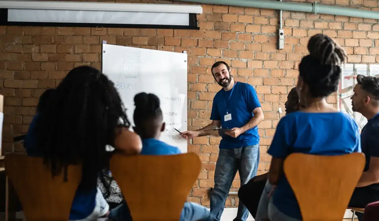A smiling instructor leads a discussion on DEI volunteer opportunities, pointing to a whiteboard with words like 