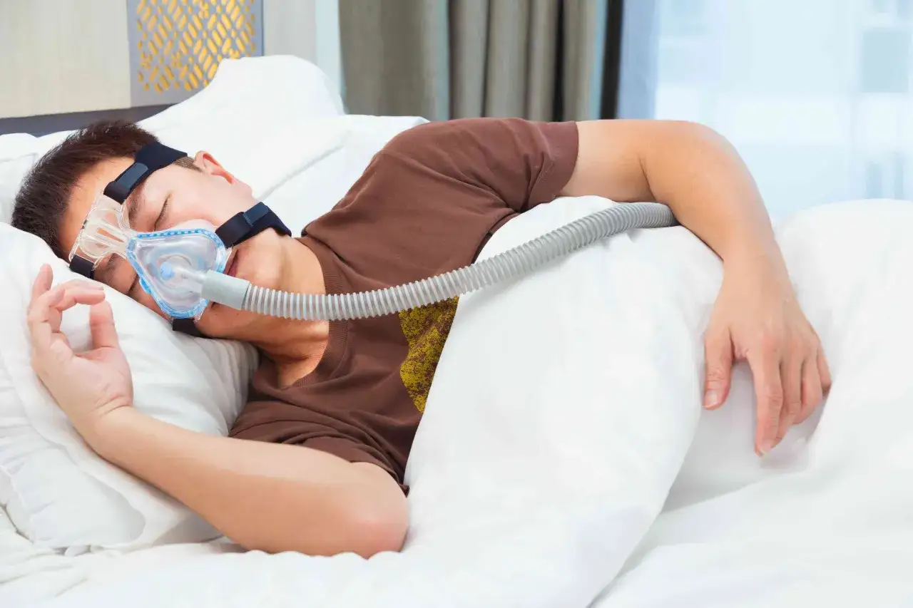 Mężczyzna śpi w masce CPAP, która pomaga mu oddychać podczas snu, łagodząc objawy bezdechu sennego.