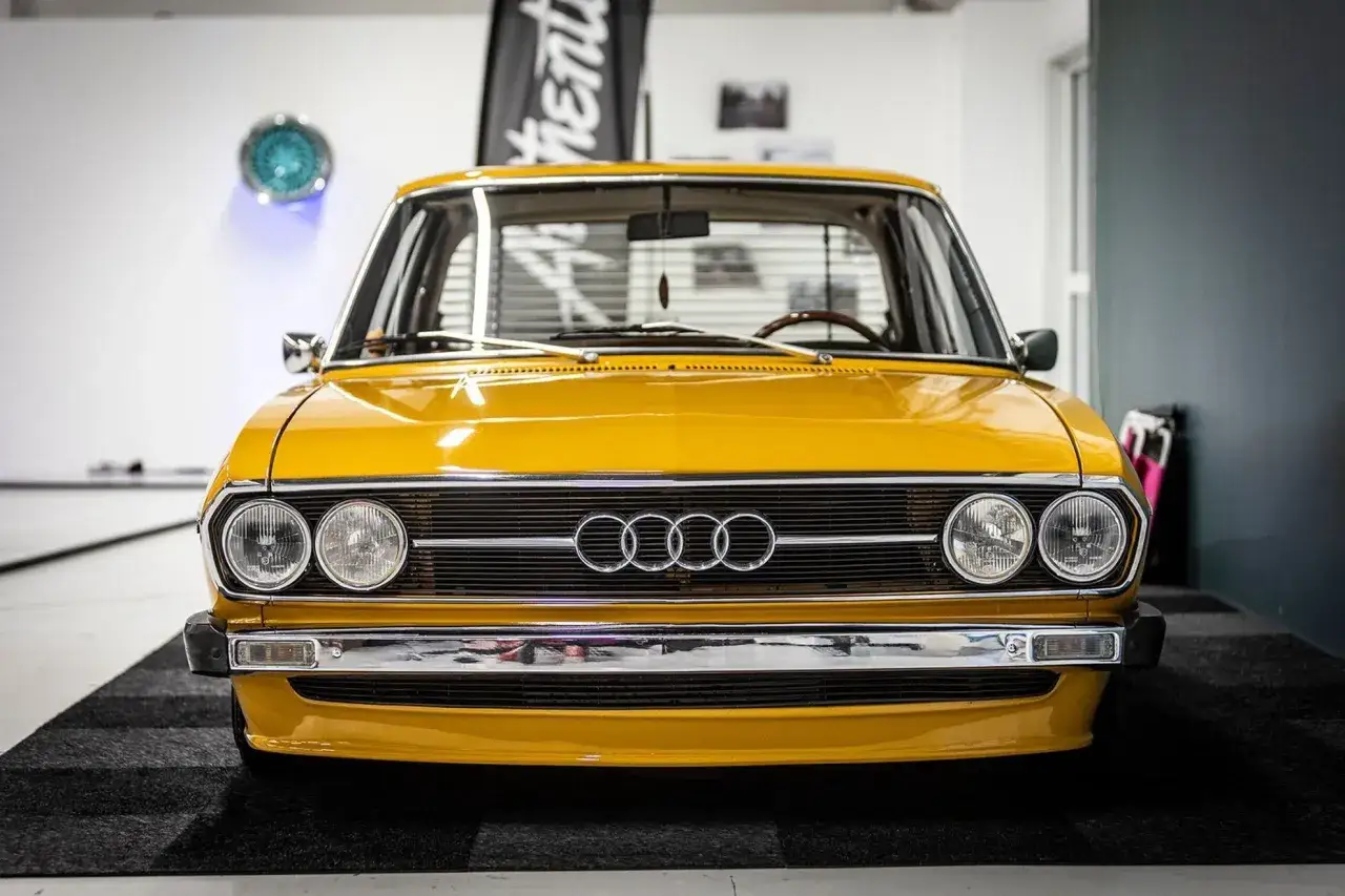 Gul Audi 100 C1 med kromdetaljer och klassiska runda str&aring;lkastare.