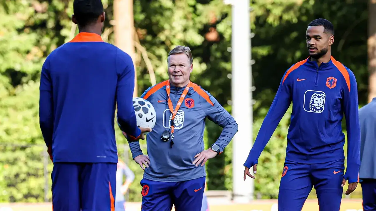 Trener Holandii, Ronald Koeman, w otoczeniu zawodników na boisku treningowym.