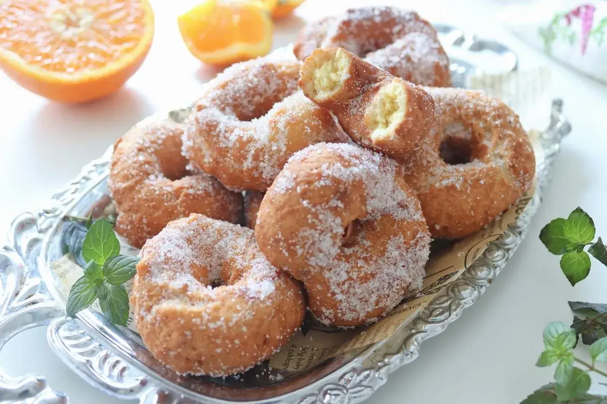 Rosquillas de naranja reci&eacute;n hechas, cubiertas de az&uacute;car, servidas en una bandeja plateada con hojas de menta.