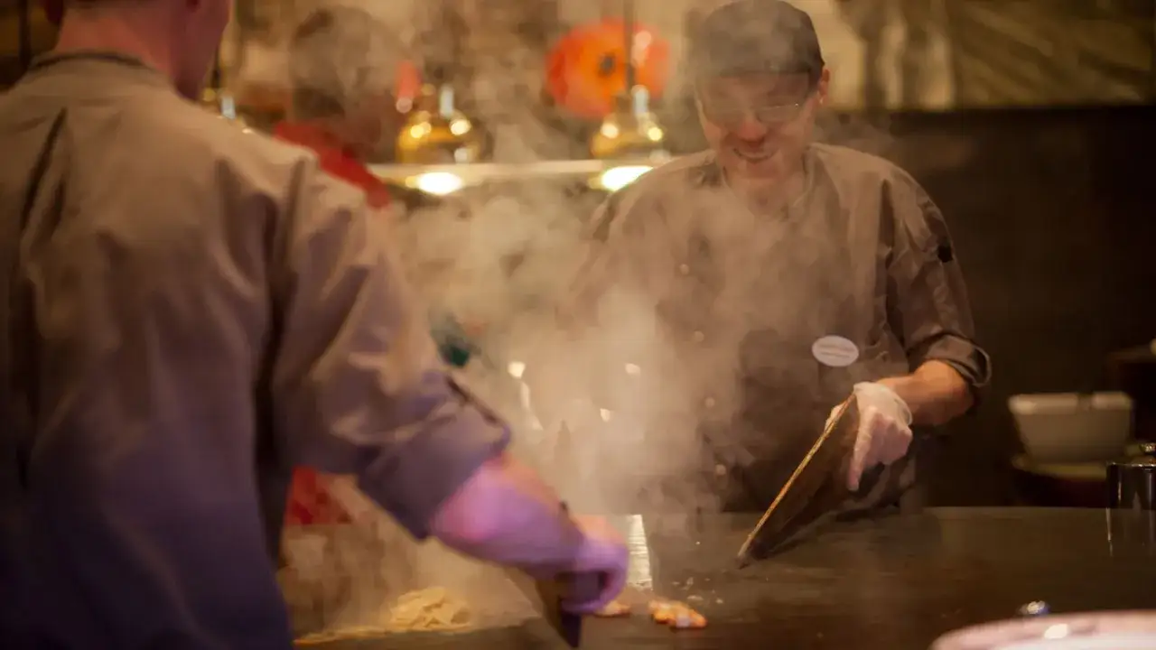 K&ouml;che bereiten im Bell Rock Buffet Speisen zu. Dampf steigt von der hei&szlig;en Platte auf, w&auml;hrend sie mit Werkzeugen arbeiten.