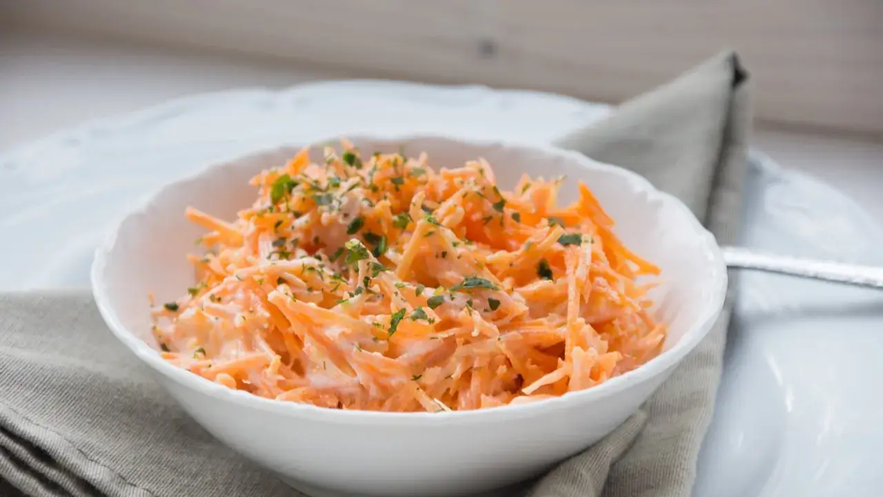 Ein erfrischender Karotten-Apfel-Salat mit Joghurt, garniert mit Petersilie, in einer wei&szlig;en Sch&uuml;ssel.