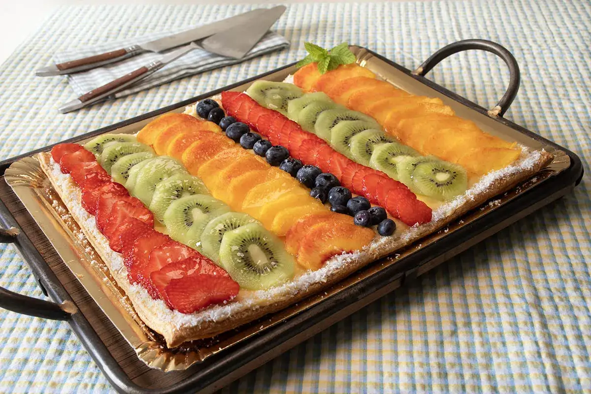 Deliciosa tarta de hojaldre cubierta con filas de fresas, kiwi, melocotón y arándanos.