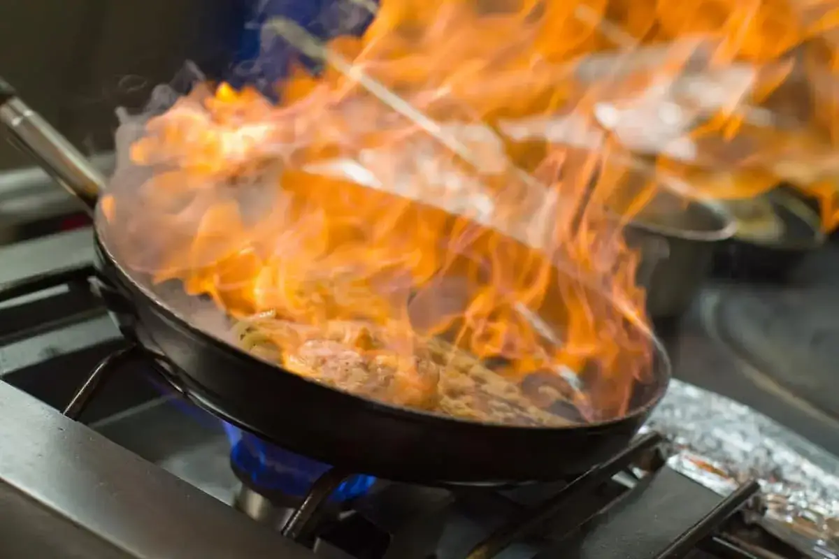 Flames licking a pan of food on a stove. This dramatic cooking technique shows how quickly cuanto tarda en evaporarse el alcohol.