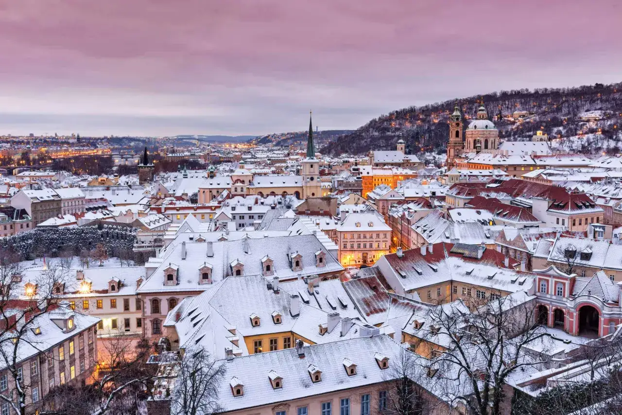 Vintervy &ouml;ver Prag med sn&ouml;t&auml;ckta tak och upplysta f&ouml;nster. En vacker prag temperatur i skymningen.