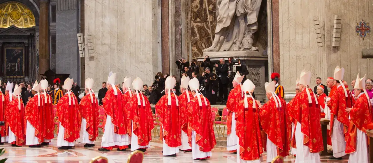 Kardinäle in roten Gewändern und Mitra stehen in einer Kirche. Dies ist ein Moment, der an ein Konklave erinnert, die Wahl eines neuen Papstes.