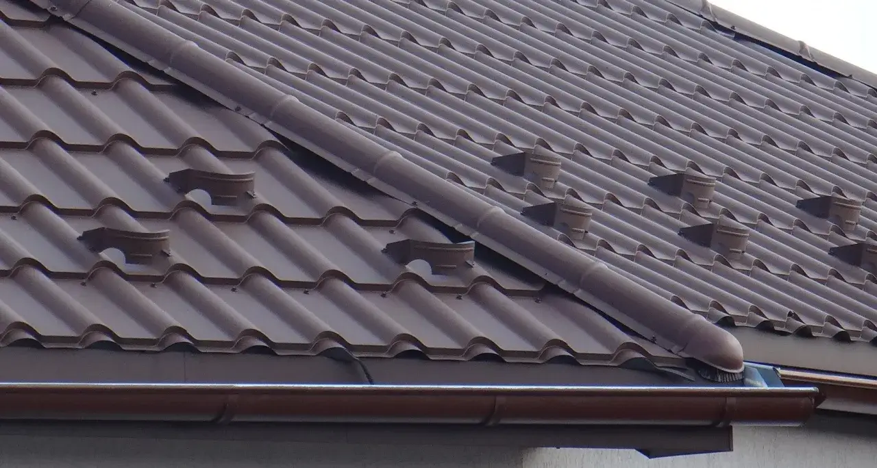 Brązowy dach z dachówki ceramicznej, widoczne są zaślepki gąsiora z blachy, które chronią przed wiatrem i deszczem.