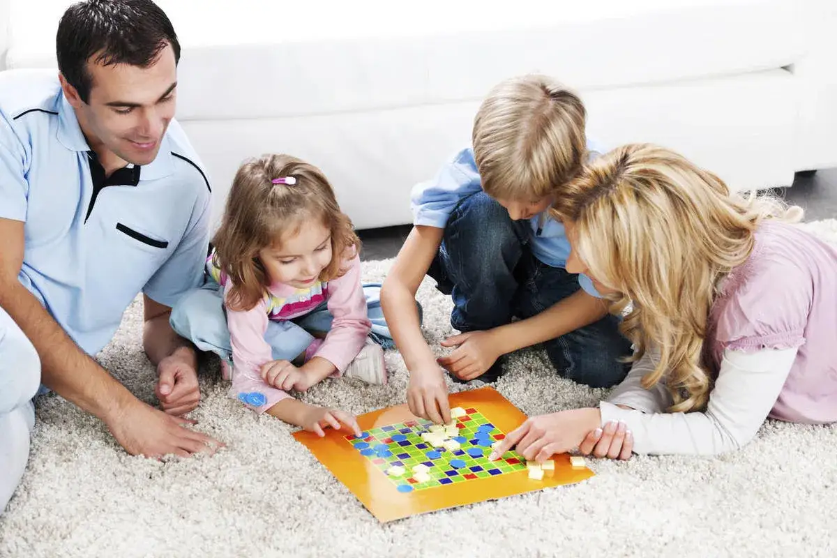 Familie spielt Brettspiel. Vater, Mutter und zwei Kinder sitzen auf dem Teppich und sind vertieft in ein spannendes **party spiel**.