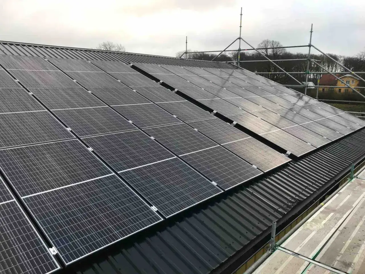 Solceller tillverkning p&aring;g&aring;r p&aring; ett m&ouml;rkt tak. St&auml;llningar syns runt taket.