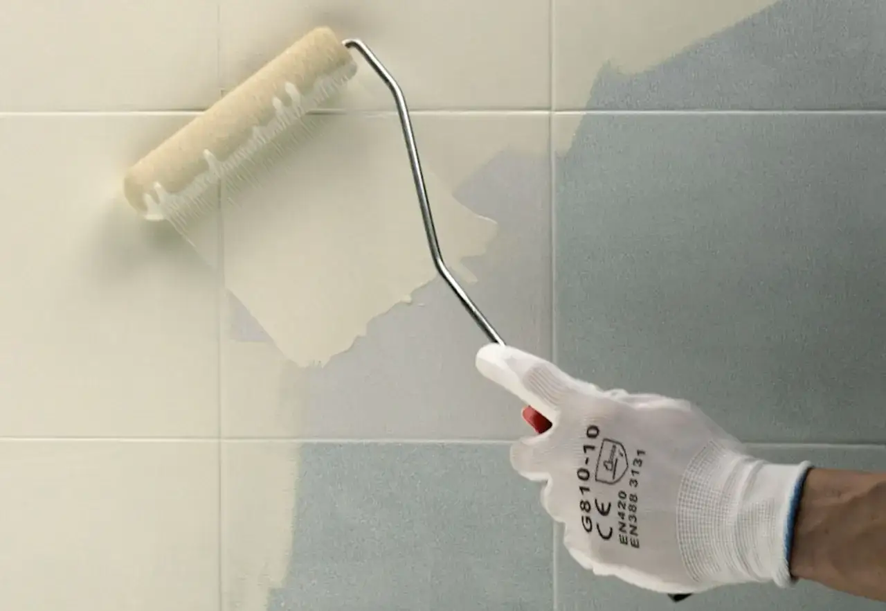Rullo applica vernice per piastrelle, trasformando le vecchie piastrelle grigie in un nuovo colore chiaro.