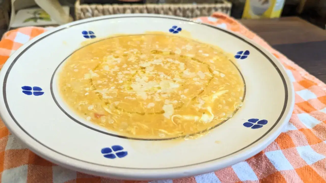 Eine dampfende Schüssel Pastina Suppe, garniert mit Parmesan und einem Hauch Olivenöl, auf einem karierten Tuch.