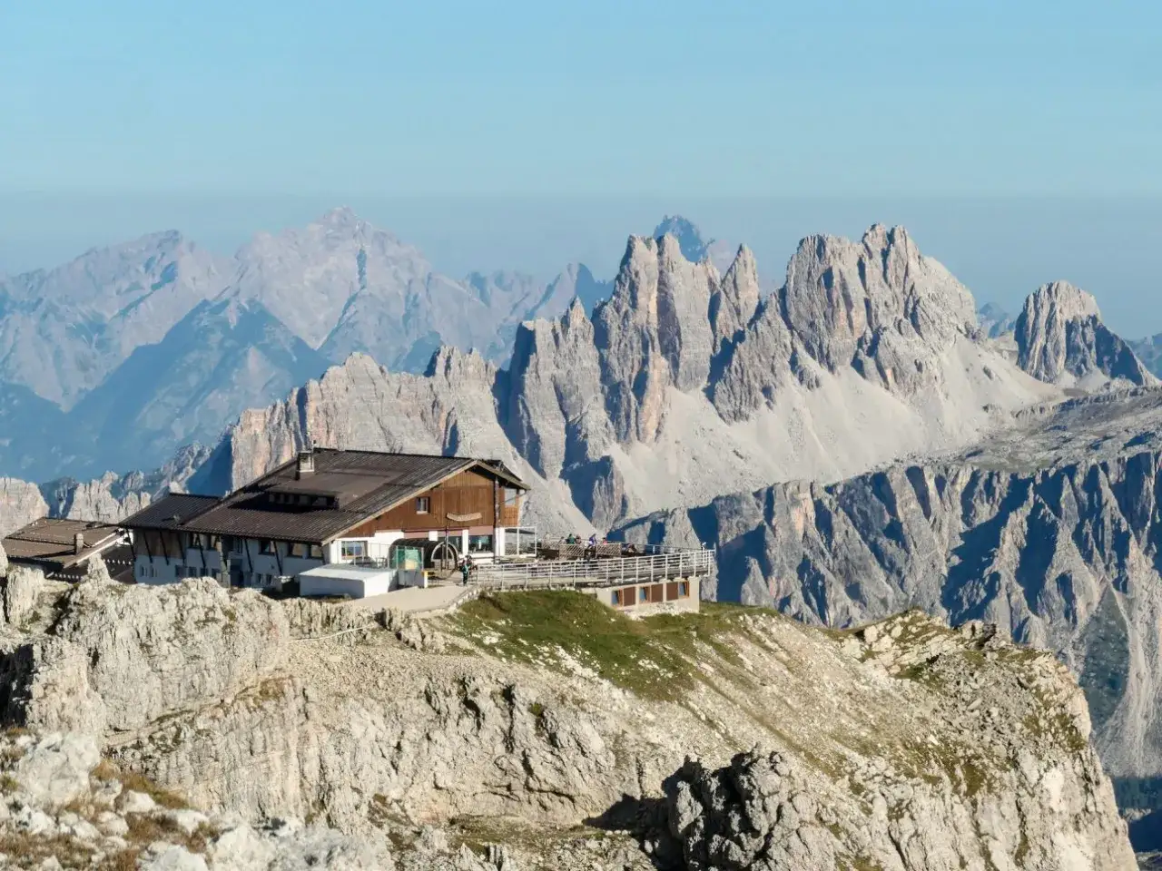H&uuml;tte auf einem Felsvorsprung mit Blick auf schroffe Gipfel. Ein perfekter Rastplatz f&uuml;r Wanderer auf den Fernwanderwegen Alpen.